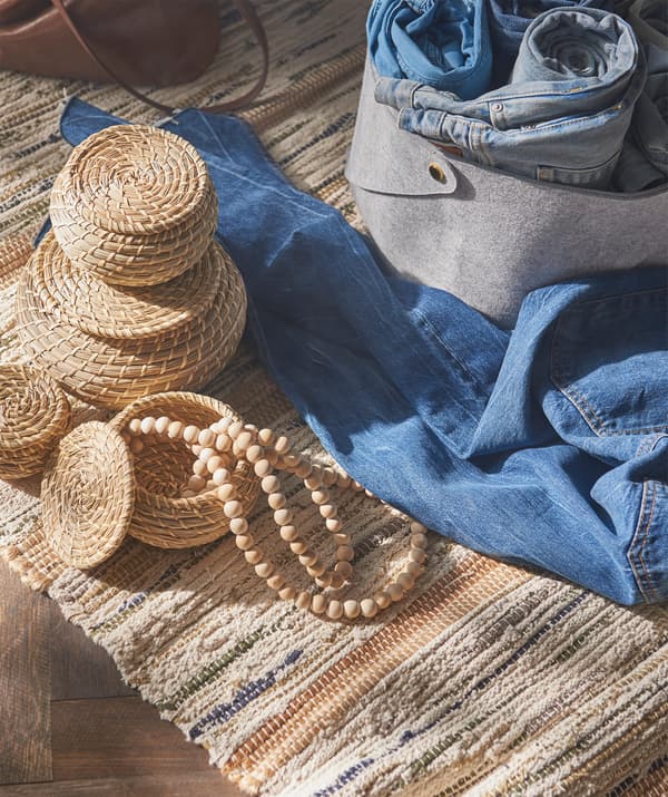 Trois petites boîtes rondes en jonc de mer à côté de plusieurs jeans et une boîte de rangement en feutre gris.