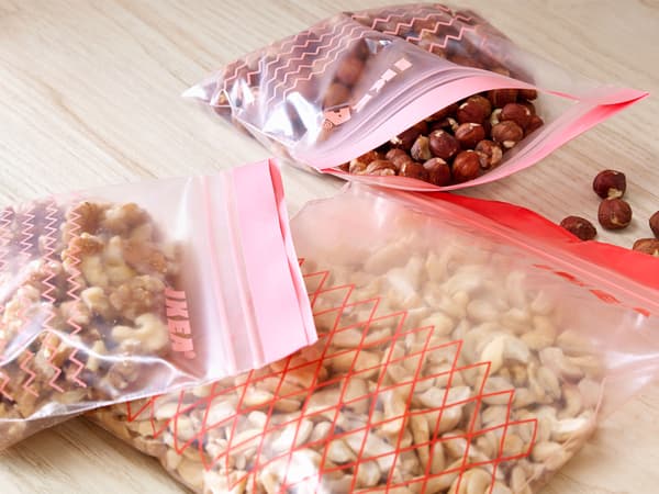 Trois sacs en plastique ISTAD contenant différentes sortes de noix sur un plan de travail en bois.