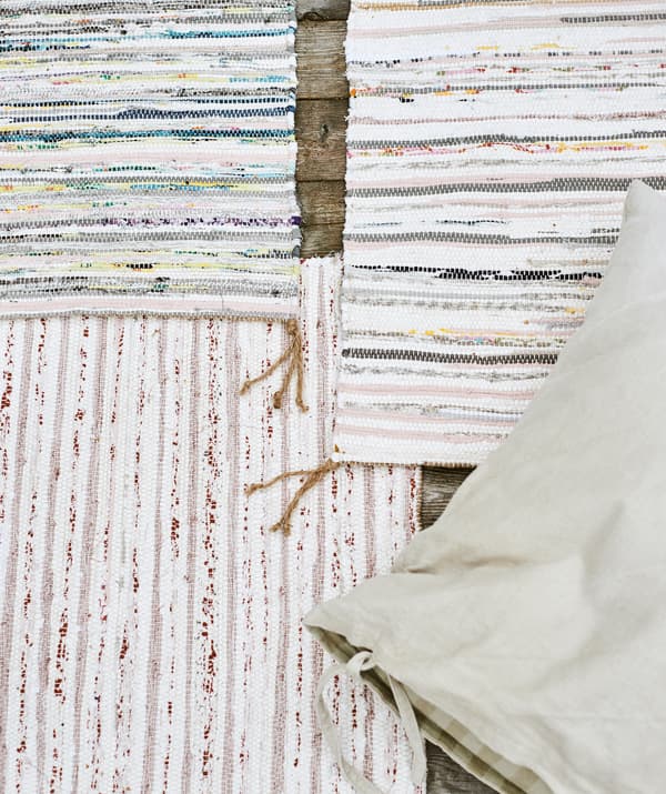 Trois tapis rayés multicolores et tissés à la main se superposent sur un ponton en bois, un coussin avec housse en lin beige sur le dessus.