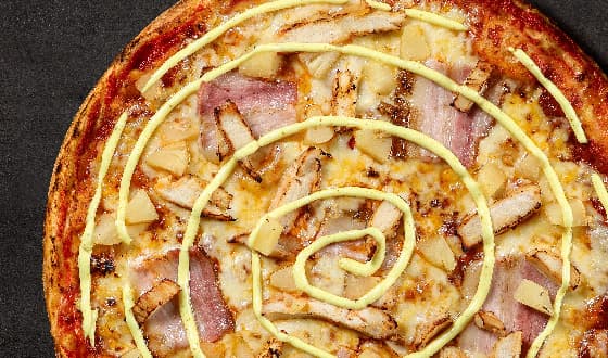 Tropical pizza with chicken, bacon, pineapple, and a spiral of curry sauce.