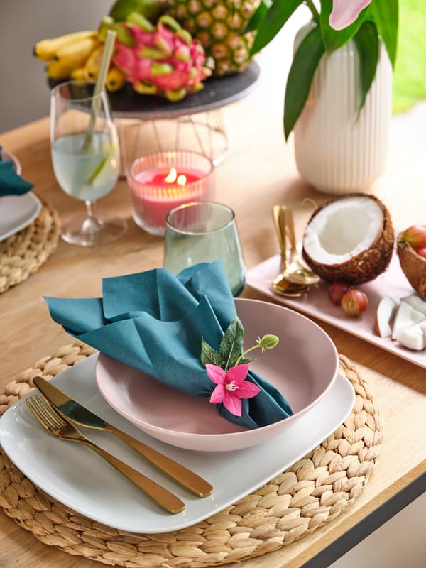 Tropical table setting with pink bowl, turquoise napkin, gold cutlery, coconut and candle.