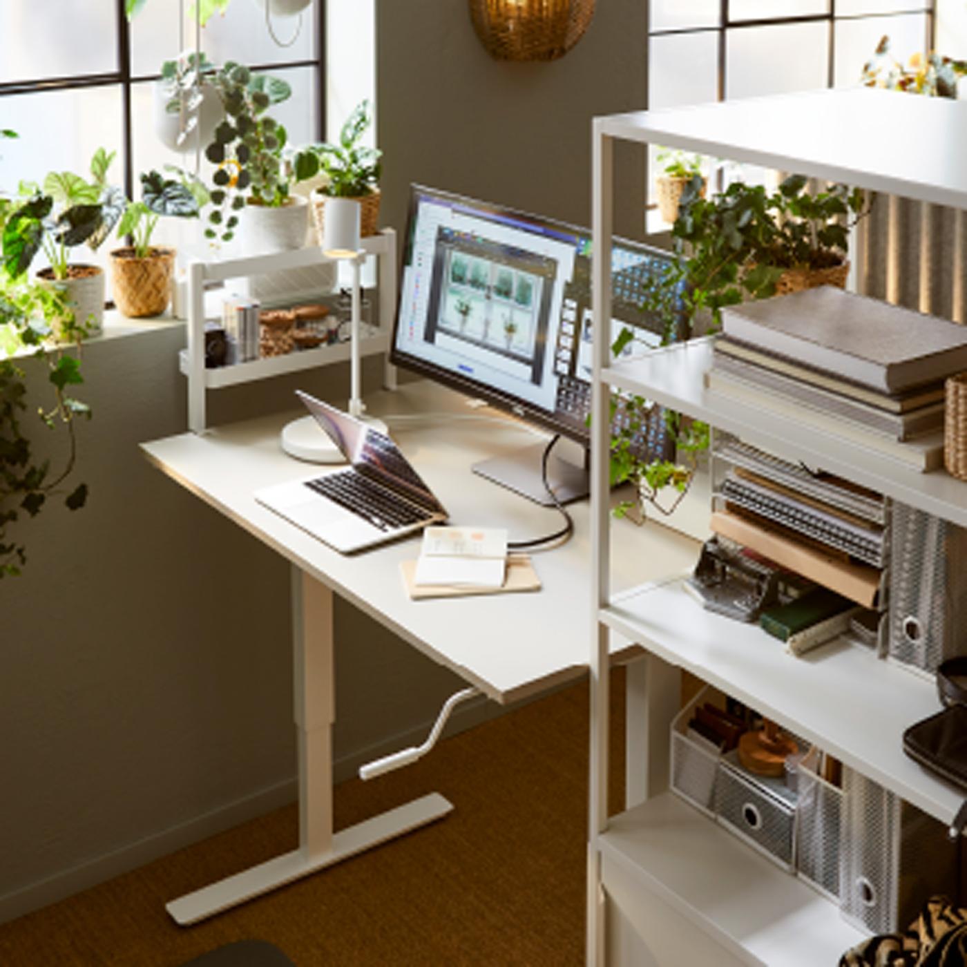 TROTTEN bureau en kast met schuifdeuren naast een raam. Aan het bureau is een VATTENKAR bureauplank met een klem bevestigd aan een plank.