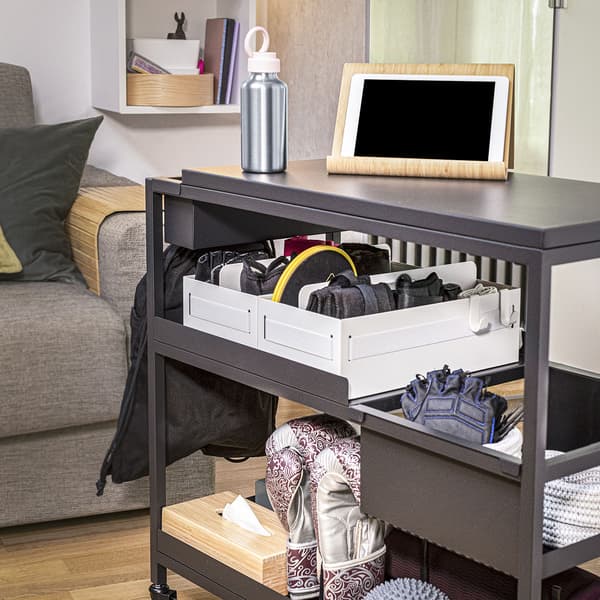 TROTTEN Carrello antracite con prodotti sportivi all'interno con un divano in sfondo. 