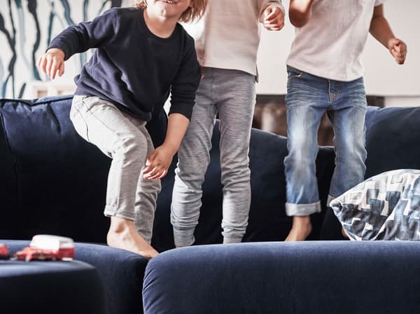Троє дітей босоніж стрибають на синьому дивані IKEA.