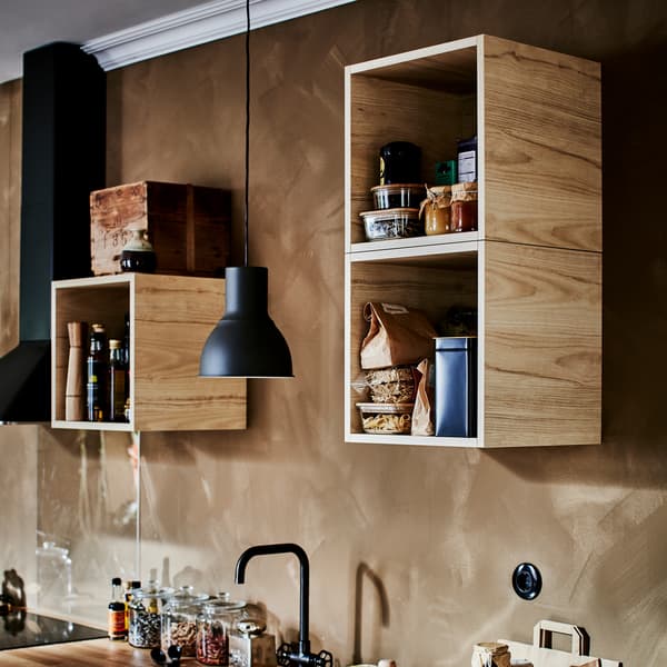 Trzy otwarte szafki ścienne wykończone okleiną jesionową, ciemnoszara lampa wisząca, czarna bateria kuchenna i czarny okap.