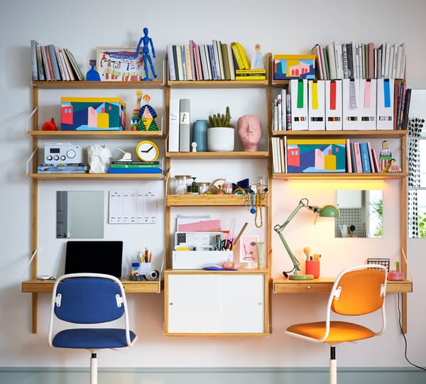 تشكيلة مساحات العمل المثبتة على الحائط SVALNÄS باللون الأبيض/الخيزران، مع الكثير من الكتب والمجلدات والأغراض الأخرى على الرفوف.