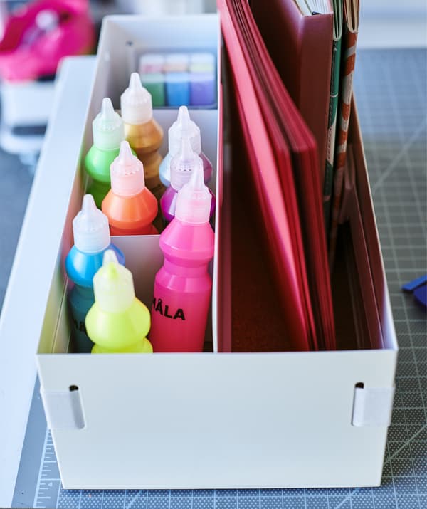 Tubes of colorful paint and notebooks stored in a white desk organizer.