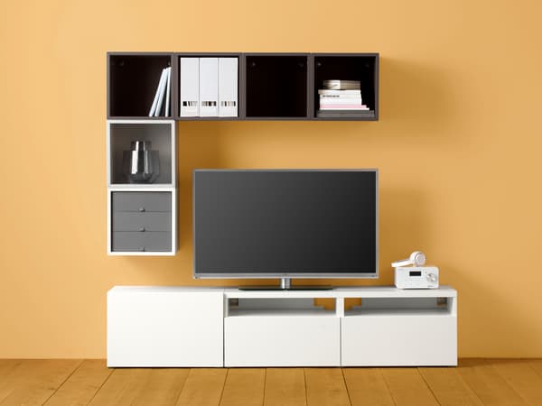 TV yang dibingkaikan di atas, di sisi dan di bawah oleh kombinasi kabinet BESTÅ dan EKET yang geometri tetapi tak simetri pada dinding berwarna kuning.