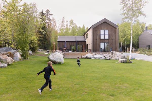 Två barn leker på en gräsmatta framför ett hus.
