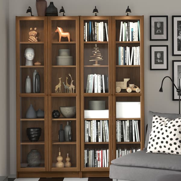 Två BILLY bokhyllor i valnöt med vitrindörrar stående mot grå vägg i ett vardagsrum där en grå soffa skymtas