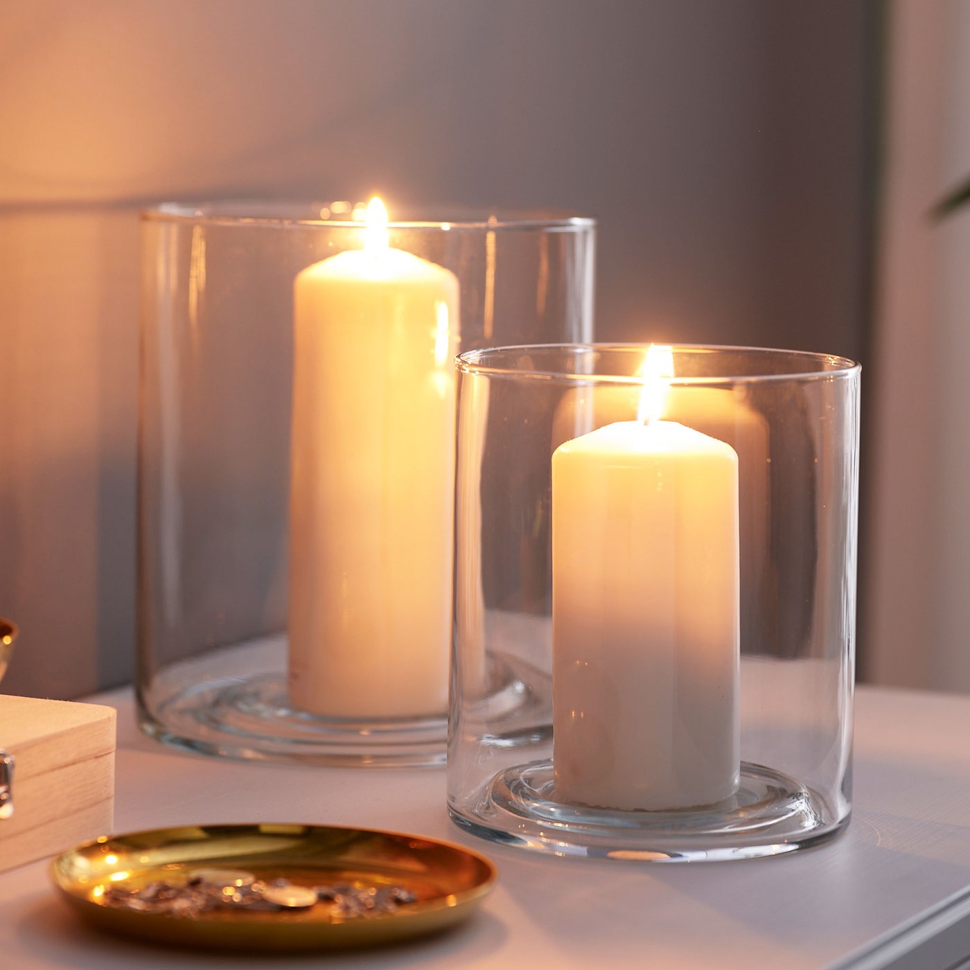 Två cylinderformade ljuslyktor i glas med vita blockljus. 