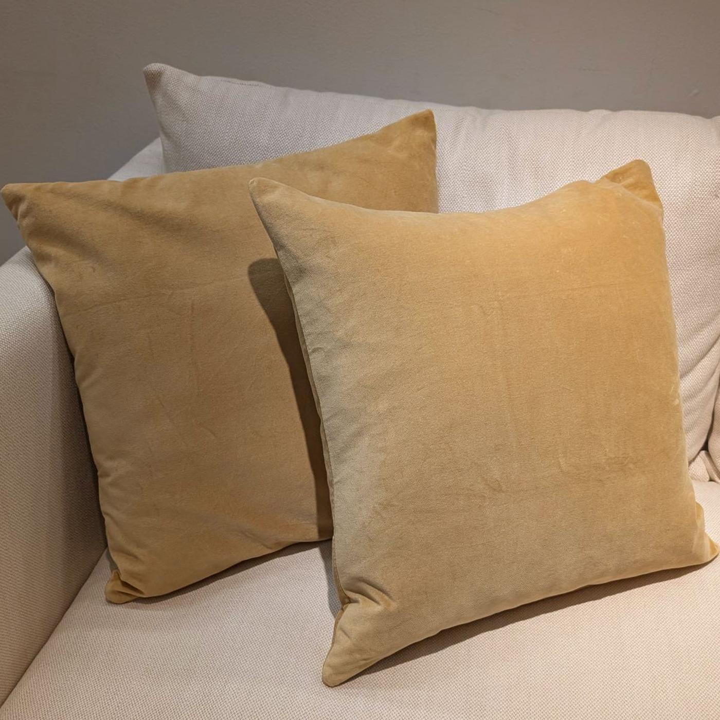 Två gulbruna SANELA sammetskuddar i storlek 50x50 cm i en ljusbeige soffa.