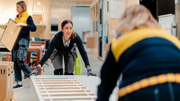 Två IKEA medarbetare hjälps åt att lyfta en madrassbotten