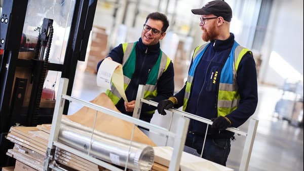 Två IKEA medarbetare klädda i säkerhetsväst står vid en truck och tittar på en lista.