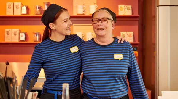 Två IKEA medarbetare som kramar om varandra och skrattar.