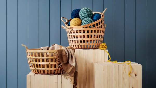Två korgar med garnnystan står framför en blå vägg. 