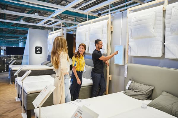 Två kvinnor varav en med IKEA-uniform står och pratar medan en man pekar på en skärm
