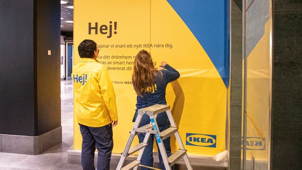 Två personer klär in en vägg med gul och blå IKEA-reklam.