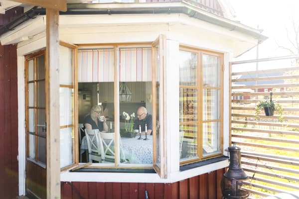 Två personer sitter i en utbyggnad av ett hus och dricker kaffe. 