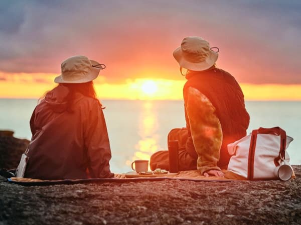 Två personer sitter på en klippa och tittar på en solnedgång över havet.