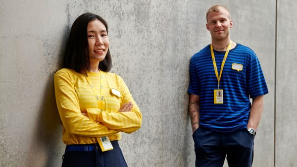 Två personer står avslappnat mot en betongvägg, iklädda blå och gula IKEA-tröjor.