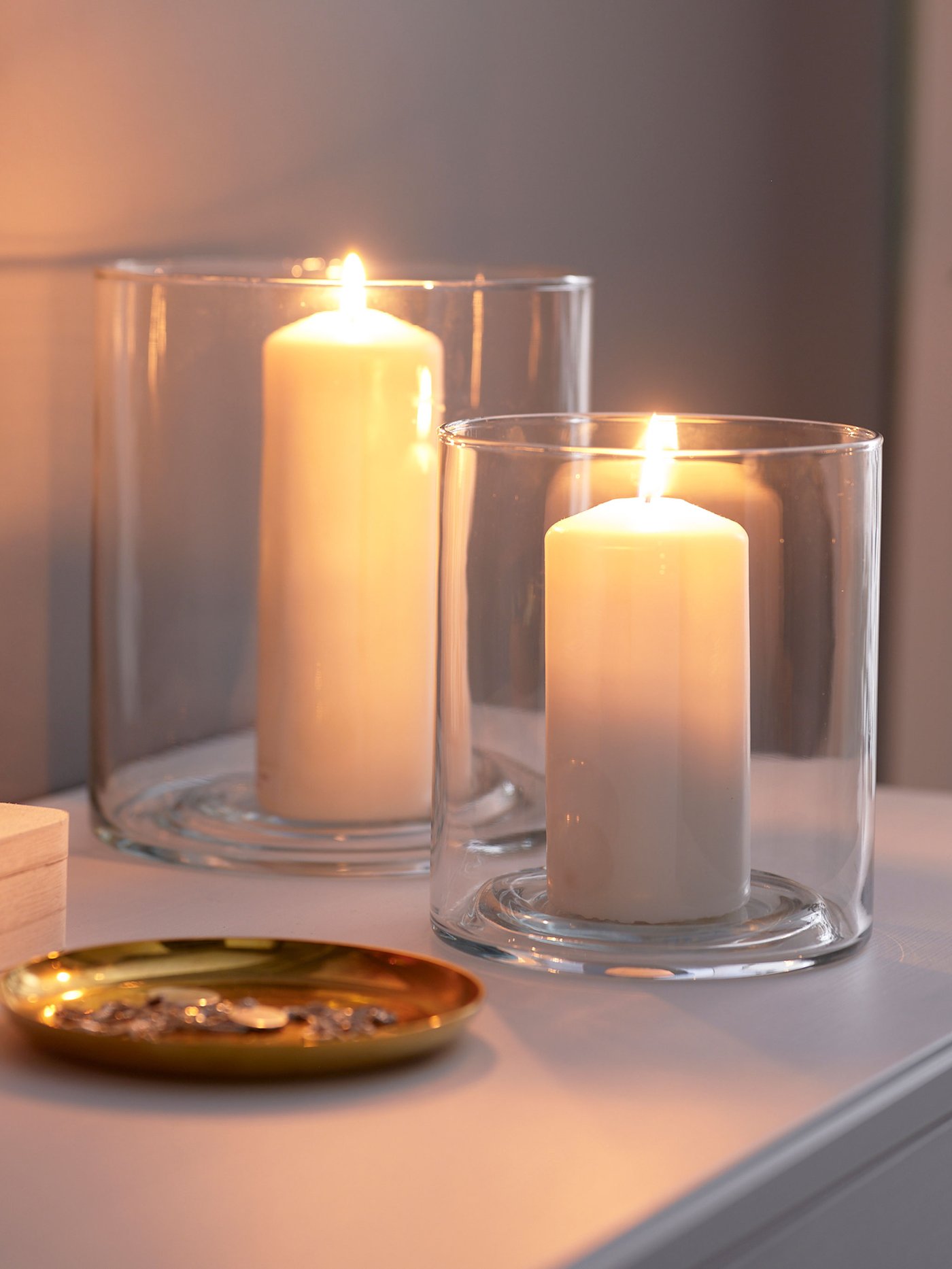 Två PILFINLK ljusttakar i glas i olika storlekar med varsitt vitt blockljus.