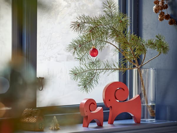Två röda julbockar i trä står i en fönsterkarm.