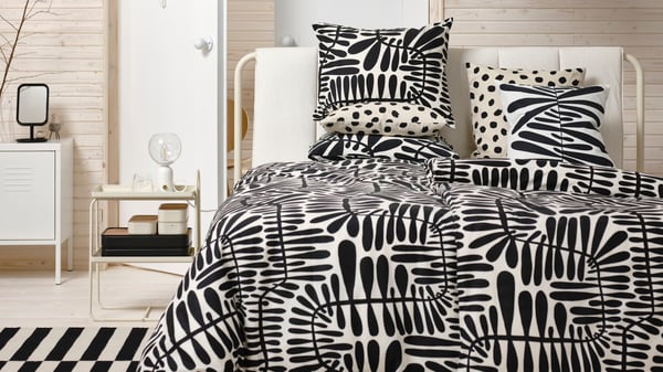 Två vita stolar står i ett rum. På stolarna ligger ett täcke och två kuddar med svartvitt mönster. 