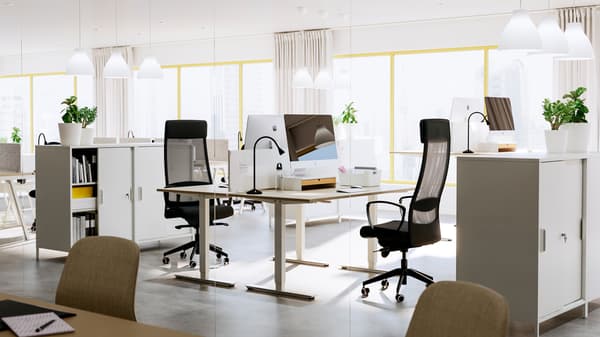 Twee beige/witte TROTTEN bureaus met donkergrijze stoelen staan in een luchtige kantooromgeving.