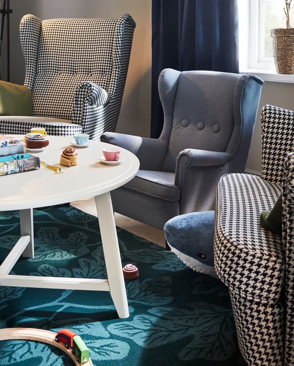 Twee oorfauteuils en een kinderfauteuil staan naast een witte ronde KRAGSTA tafel met speelgoed op het tafelblad.
