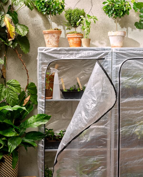 Twee rekken met bekleding uit kunststof, bij één is de bekleding open en zie je kleine plantjes op de schappen. Bovenop de schappen staan een aantal planten.