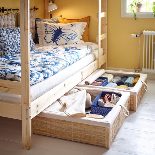 Twee rotan IKEA RÖMSKOG bedlades met kleren van onder het stapelbed getrokken.