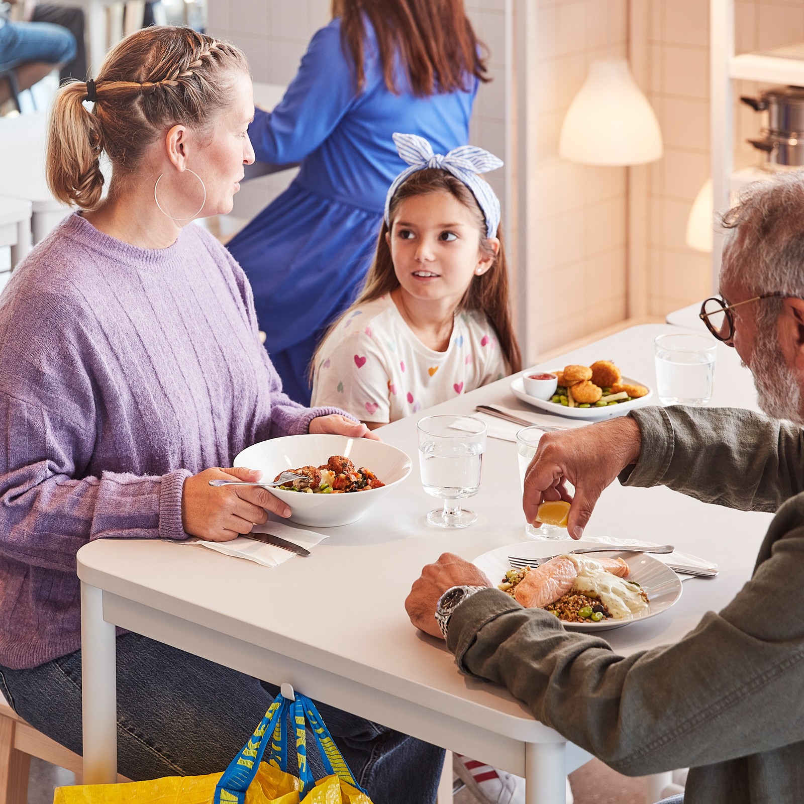 Two adults and a child about to enjoy a meal together while seated at a white table in an IKEA Swedish Restaurant.