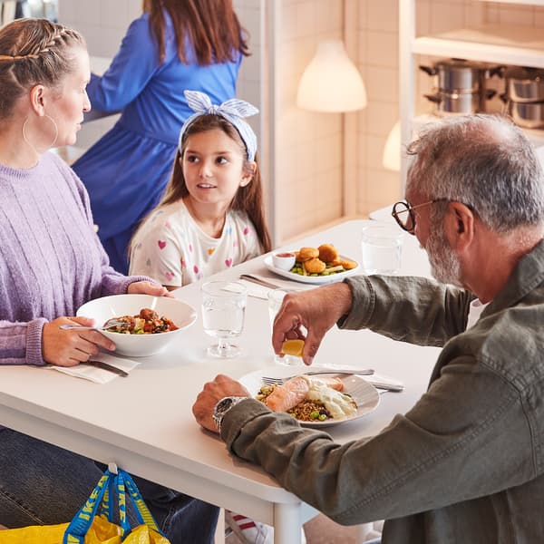 Two adults and a child about to enjoy a meal together while seated at a white table in an IKEA Swedish Restaurant.