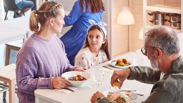 Two adults and a child about to enjoy a meal together while seated at a white table in an IKEA Swedish Restaurant.