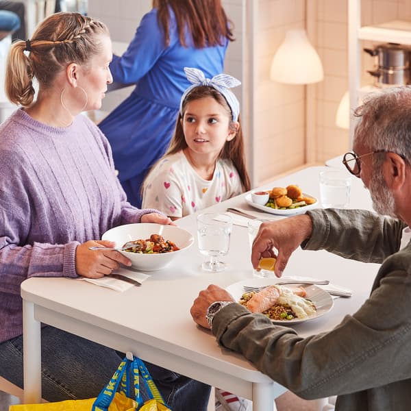Two adults and a child about to enjoy a meal together while seated at a white table in an IKEA Swedish Restaurant.
