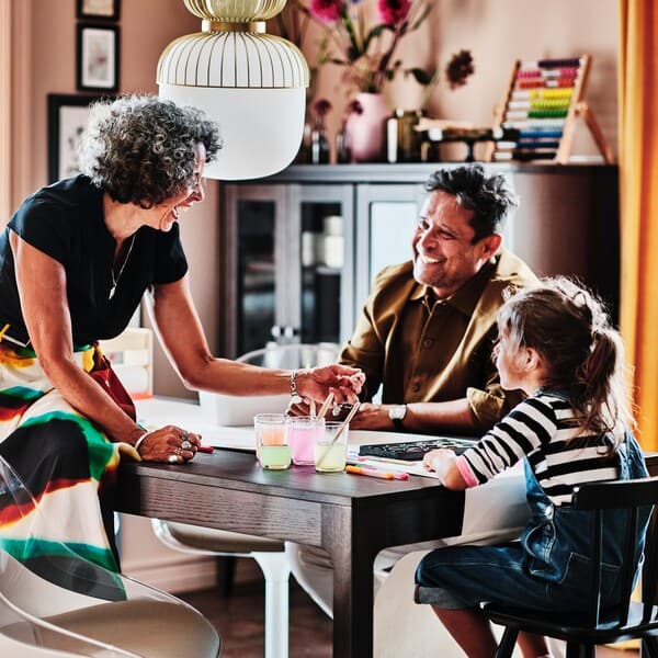 Two adults and a child around a dark brown EKEDALEN extendable table. The child sits on a black AGAM junior chair.