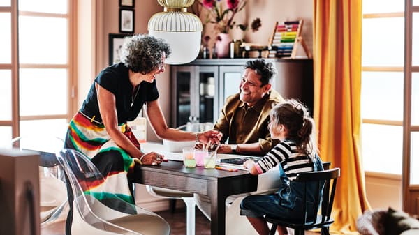 Two adults and a child around a dark brown EKEDALEN extendable table. The child sits on a black AGAM junior chair.