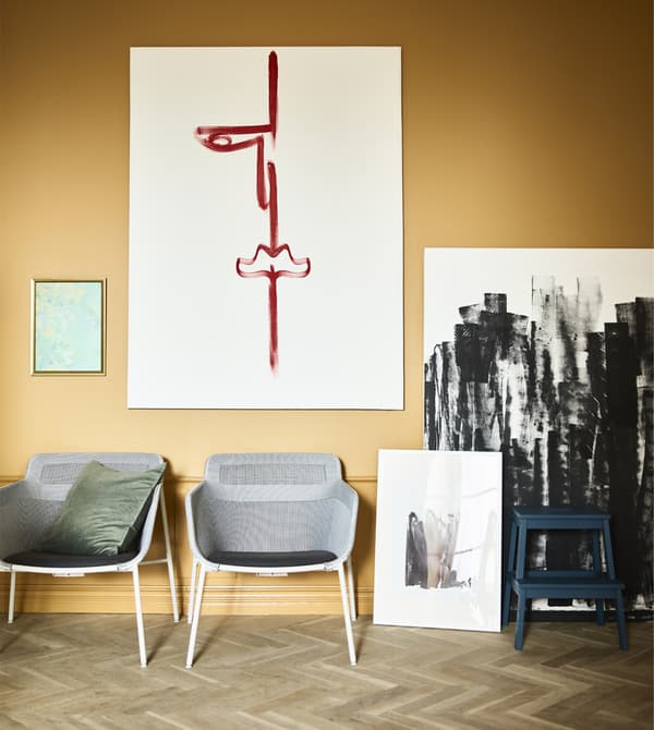 Two armchairs and canvases of art sit against a wall.