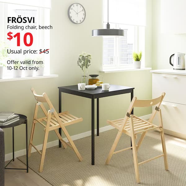 Two beech FRÖSVI folding chairs tucked into black dining table in dining room. Usual price with slash: $45. 10.10 price: $10. IKEA Alexandra birthday sale, 10.10 sale