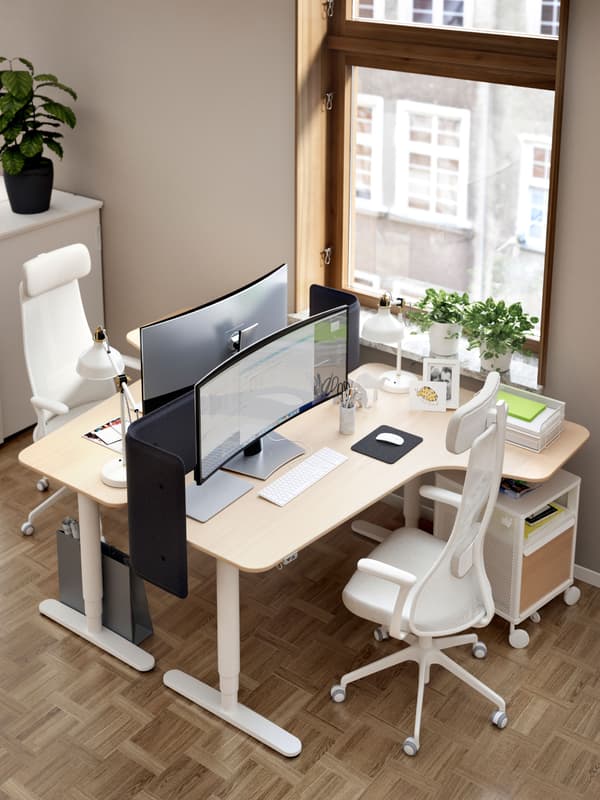 Two BEKANT corner desks facing each other beside a large window. Each desk has a JÄRVFJÄLLET chair and a BEKANT storage unit.