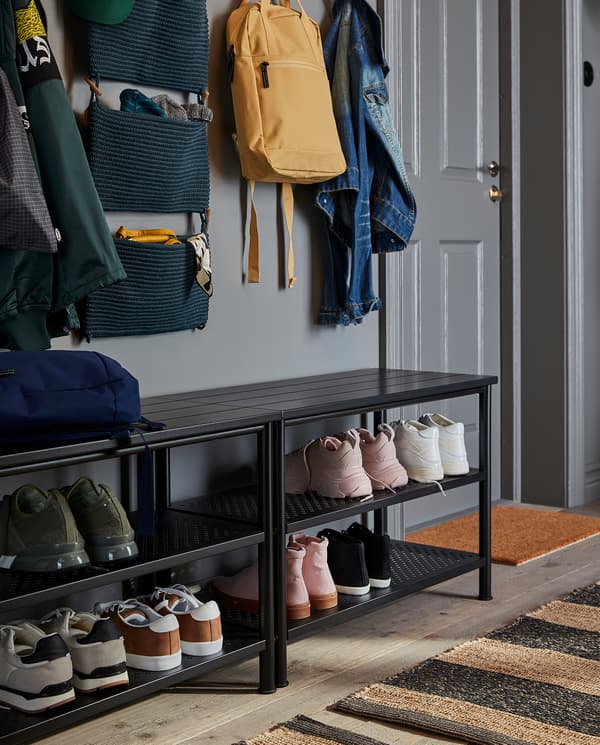 Two benches with shoe storage stand next to each other. Many shoes are stored on the shelves and jackets and bags hang above.
