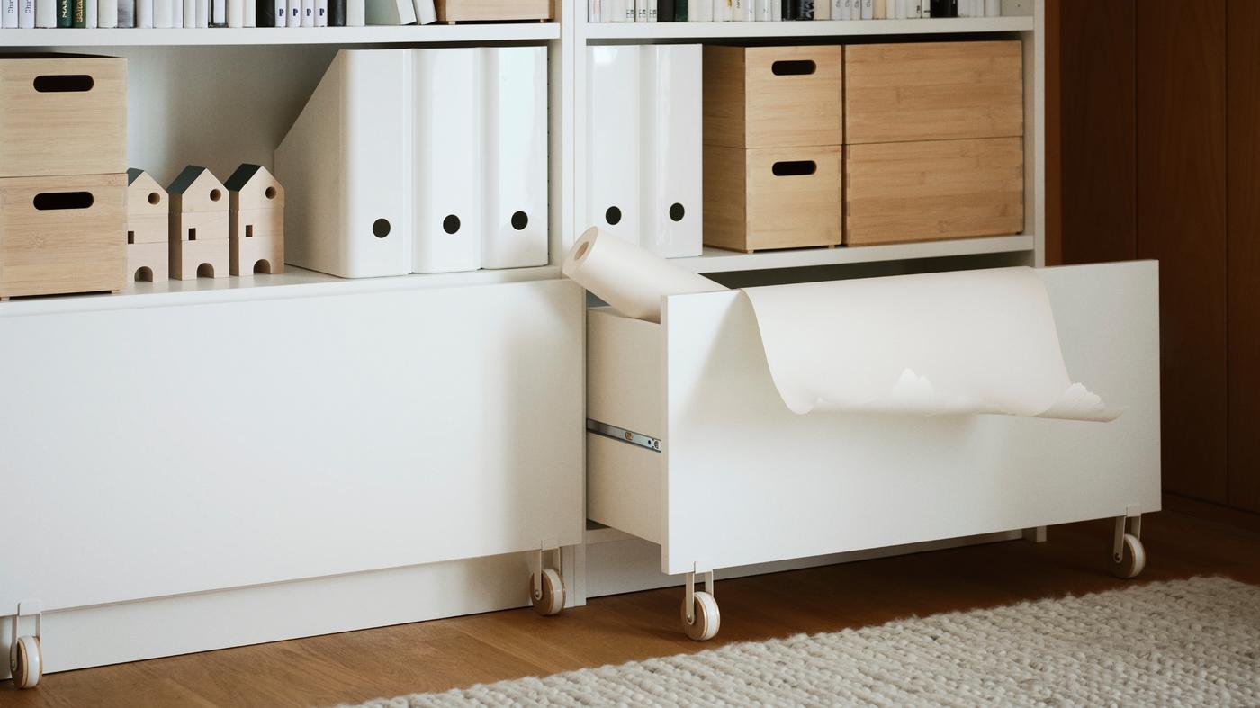Two BILLY bookshelves have folders and decorative items on them, with a drawer half open and a roll of paper hanging out.