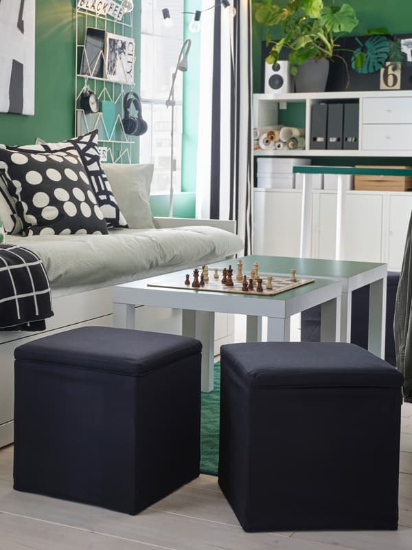 Two black footstools stand by two side tables and a day-bed and offer extra seating. A chessboard is on the table.