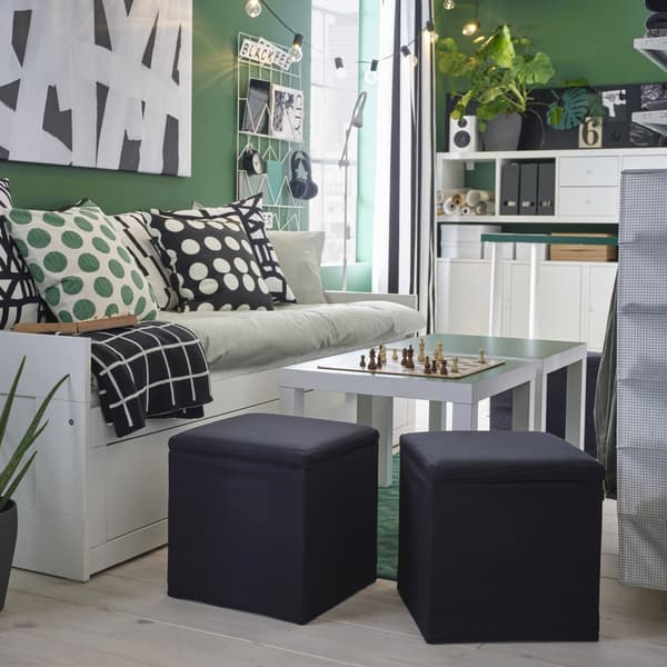 Two black footstools stand by two side tables and a day-bed and offer extra seating. A chessboard stands on the table.