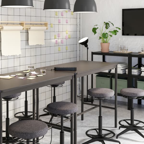 Two black high tables and several black high stools standing together, shown next to a white wall and colourful sticky notes.
