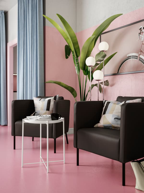 Two boxy, modern-styled EKERÖ armchairs in black leather-like fabric sit by a round tray table in a pink room.