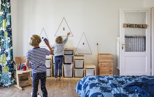 Two boys playing in a room with toy storage units against the wall.