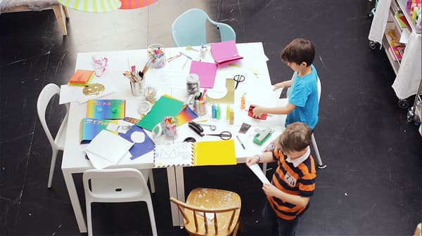 two boys working at a white square table covered in colorful arts and craft supplies