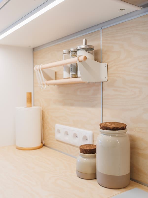 Two ceramic jars and a paper towel holder on a wooden kitchen countertop, with a NEREBY wall shelf positioned between the wall and base cabinets.